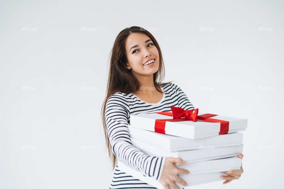 Portrait of young smiling asian woman with stack of gift boxes in hands on white background isolated
