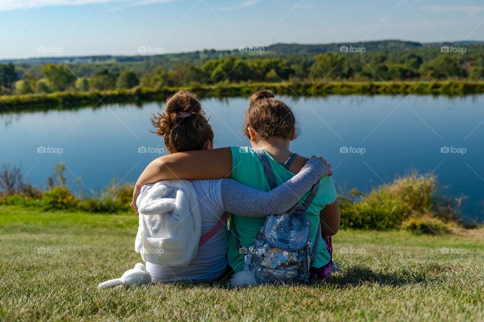 Sisters hugging each other on a pretty day by a lake in the summer 