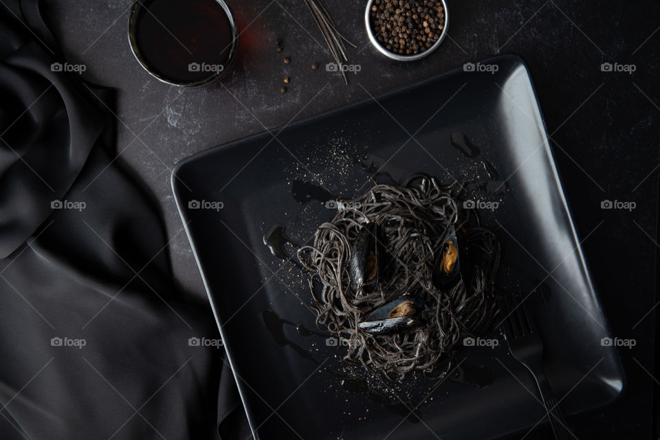 Monochromatic flat lay of a black plate of black bean spaghetti and mussels