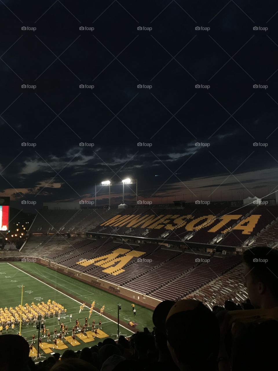 University of Minnesota football stadium at dusk, with marching band on field below