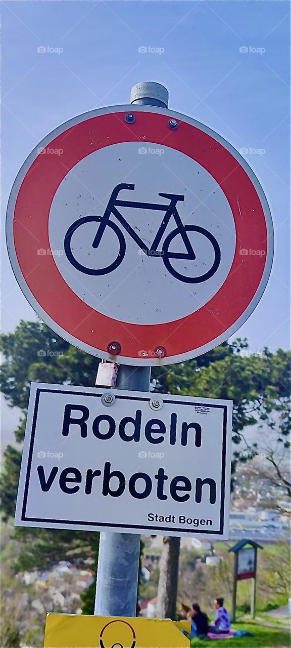 The traffic sign in the small township of “Bogen” in “Bavaria”, Germany indicates that bicycling is allowed whereas riding one’s sled in the winter isn’t which is ironic especially since the terrain is perfect for sleds. 2024. Hypnotic Productions