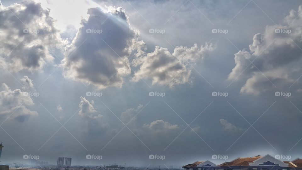 Sun rays beaming down over cityscape on cloudy sky