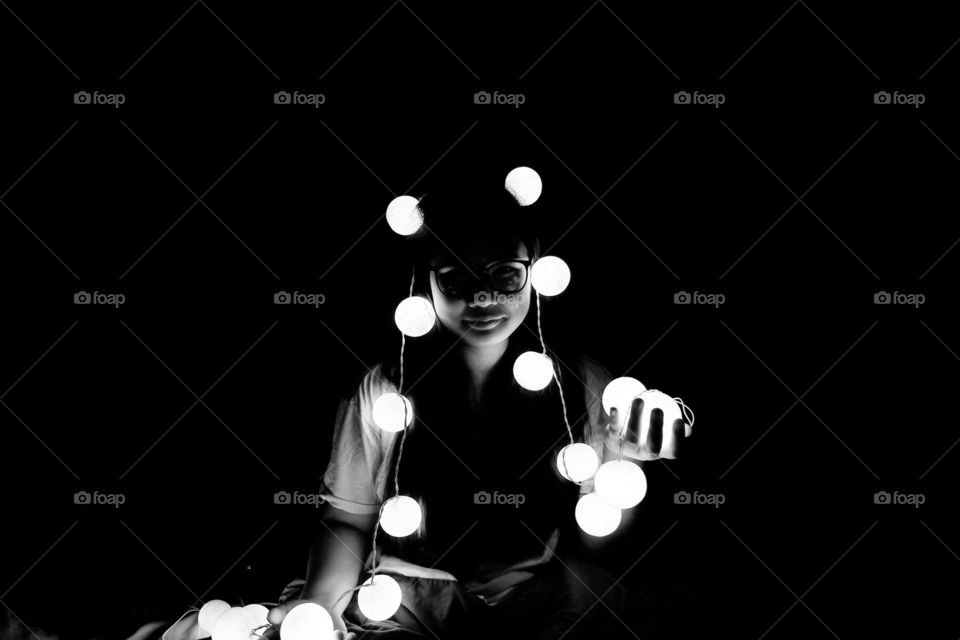 Girl hiding under lights in the dark black and white room.