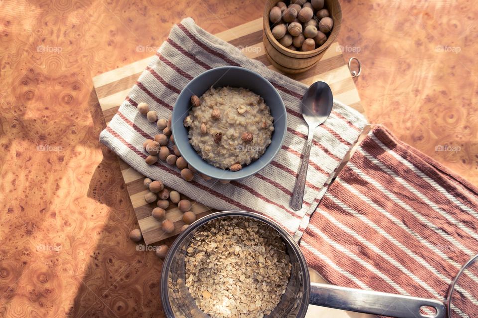 Cooked oatmeal in a deep gray plate with hazelnuts and honey.