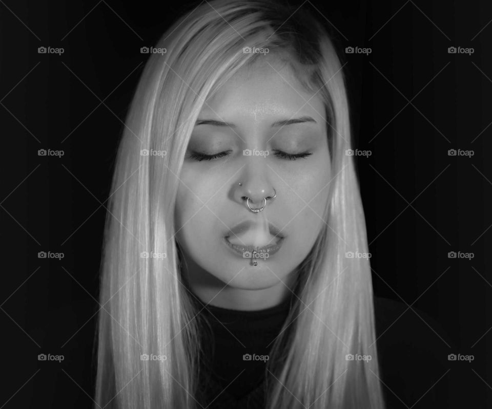 young woman with nose rings and lips playing with cigarette smoke