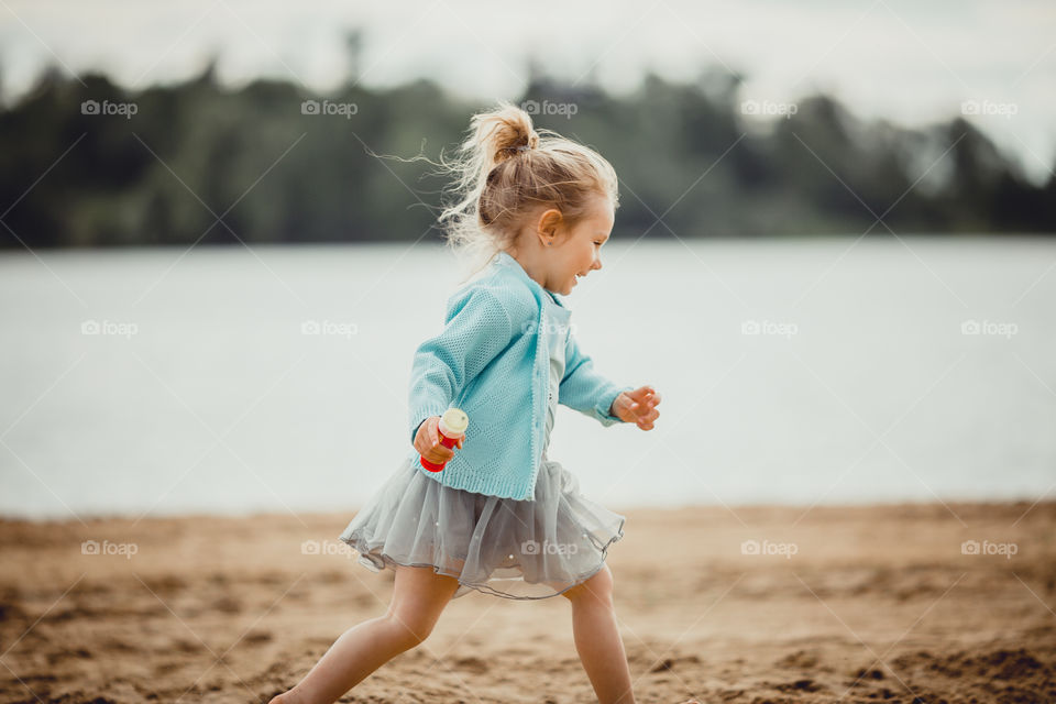 Little girl on lake coast at sunny evening. 