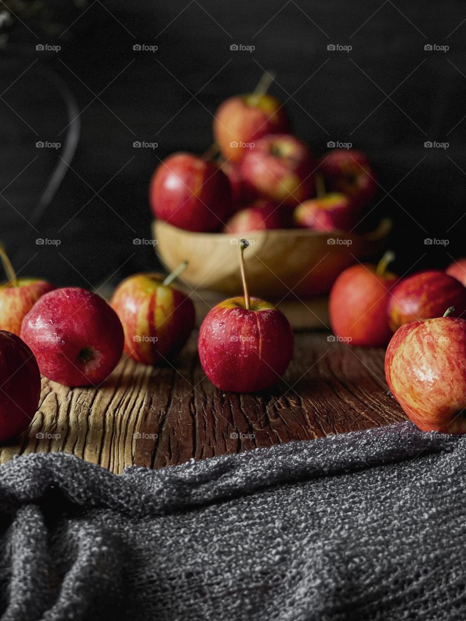 Scattered red apples on a wooden table and some in a wooden bowl