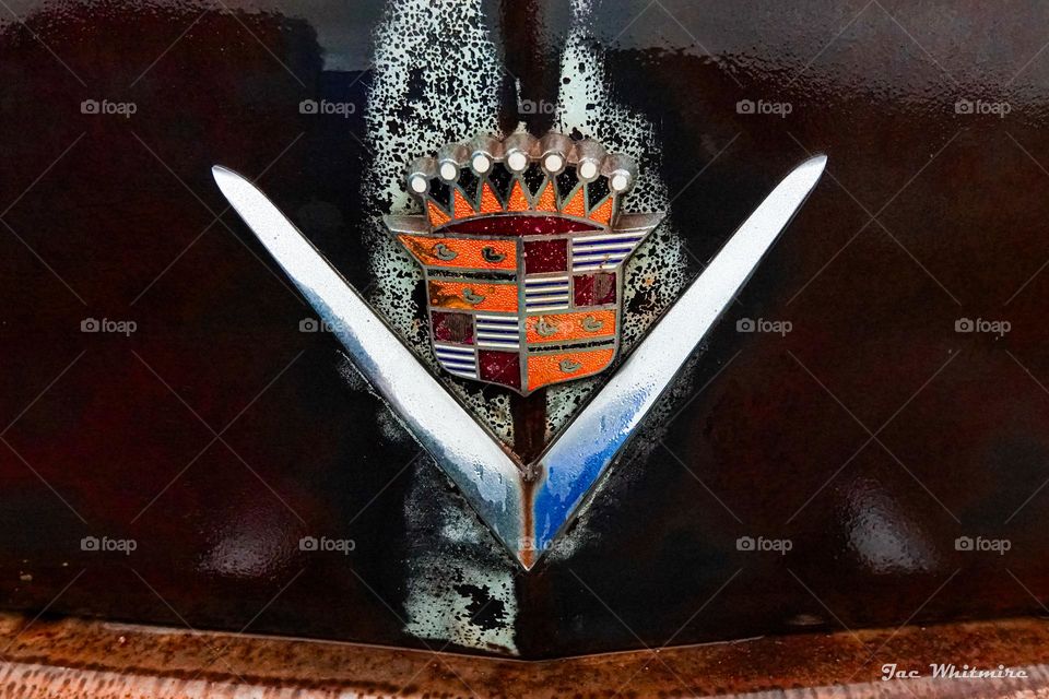A worn and weary Cadillac from the 1950's wears a polished badge featuring multiple triangles that is much better than the car it is affixed to