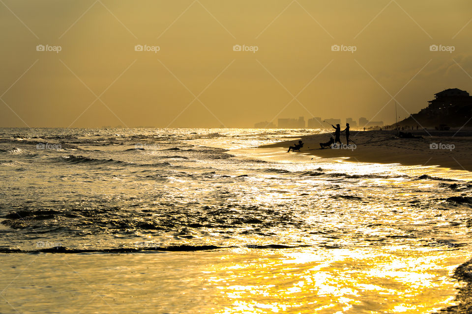 Sunset at Miami Beach, Florida. Sunlight reflecting from the ocean with orange and yellow skies while people are fishing at the beach. 