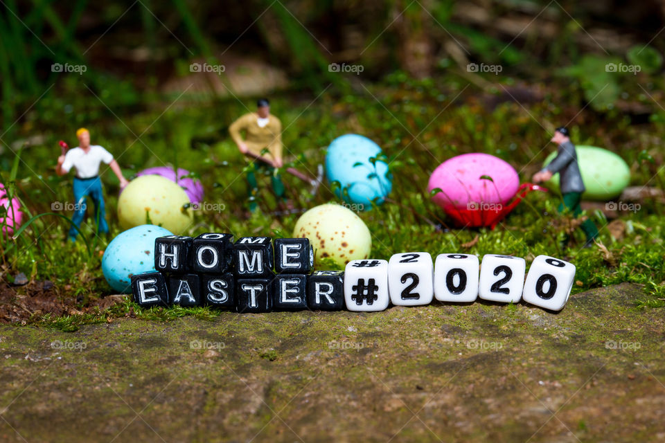 Easter at home 2020 - mini scene of 'Easter egg production' in the garden with mini construction workers, colorful easter eggs and words with home Easter 2020. Taken on a bed of moss on a rock in the backyard.