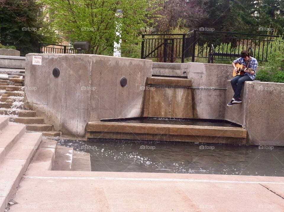 This musician decided to enjoy the summer by a fountain on beautiful university grounds.