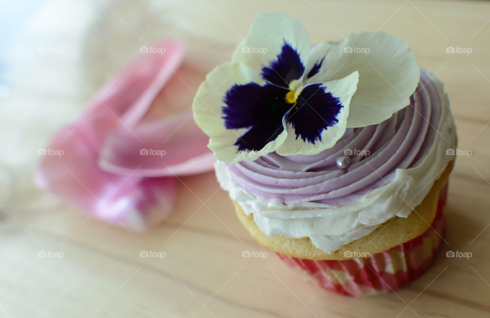Beautiful delicate floral artisanal cupcake on wood table with pink flower petals decorated with vanilla buttercream frosting and edible flower 