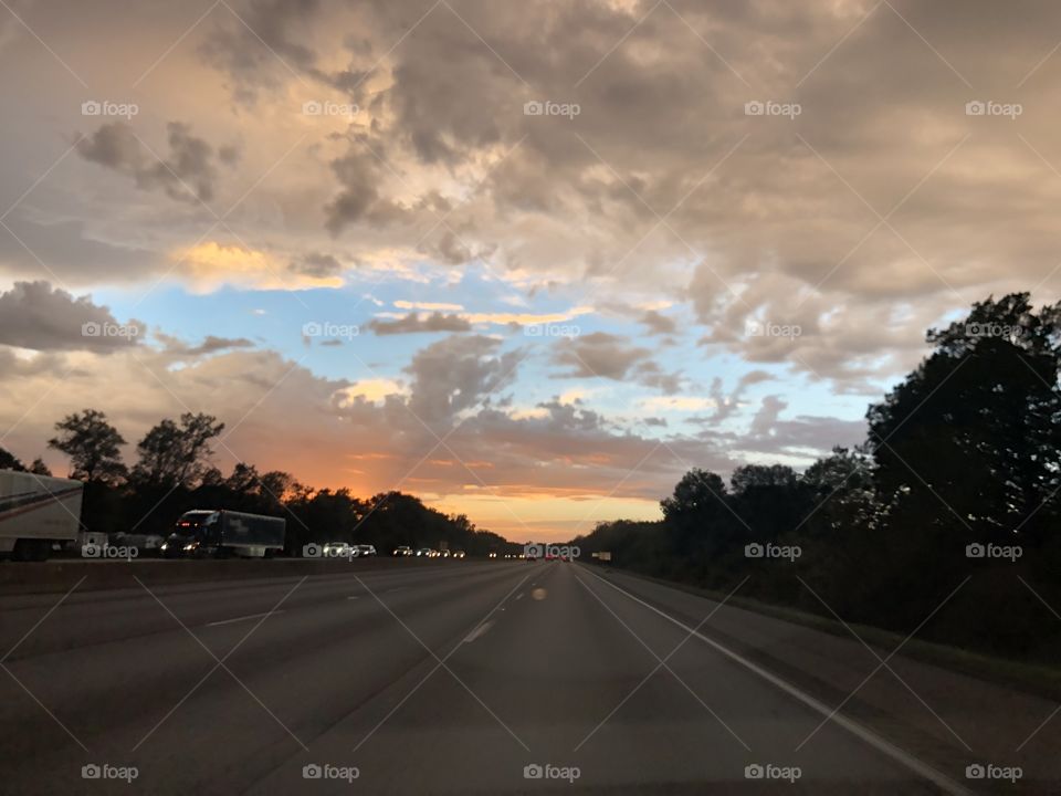 Beautiful sunset while driving on the highway. Beautiful green trees, fluffy clouds and marvelous sunset!  