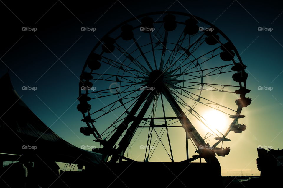 It's such a romantic experience to ride on a Ferris wheel at sunset. An elevated view of the carnival lights and crowds of people while screams and laughter of children (and adults being children) can be heard.
This hot was taken with a Nikon D5100 and post-processed through Lightroom 5. No tripod as used during this shot, as there were too many people rushing by, making their way to their next thrilling ride. Although the Ferris wheel is a slow ride, it will always be a favourite.