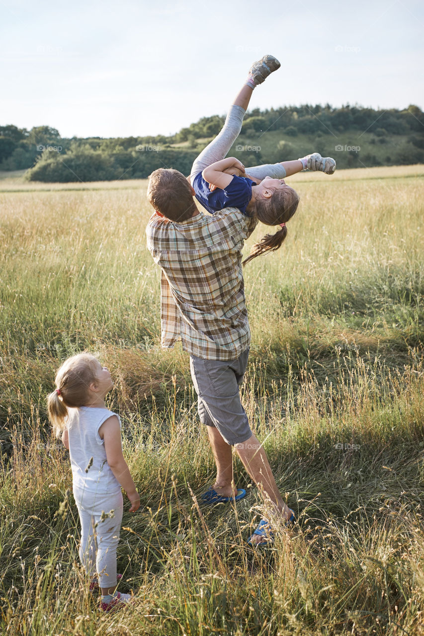 Father tossing little girl in the air. Family spending time together on a meadow, close to nature. Parents and children playing together. Candid people, real moments, authentic situations