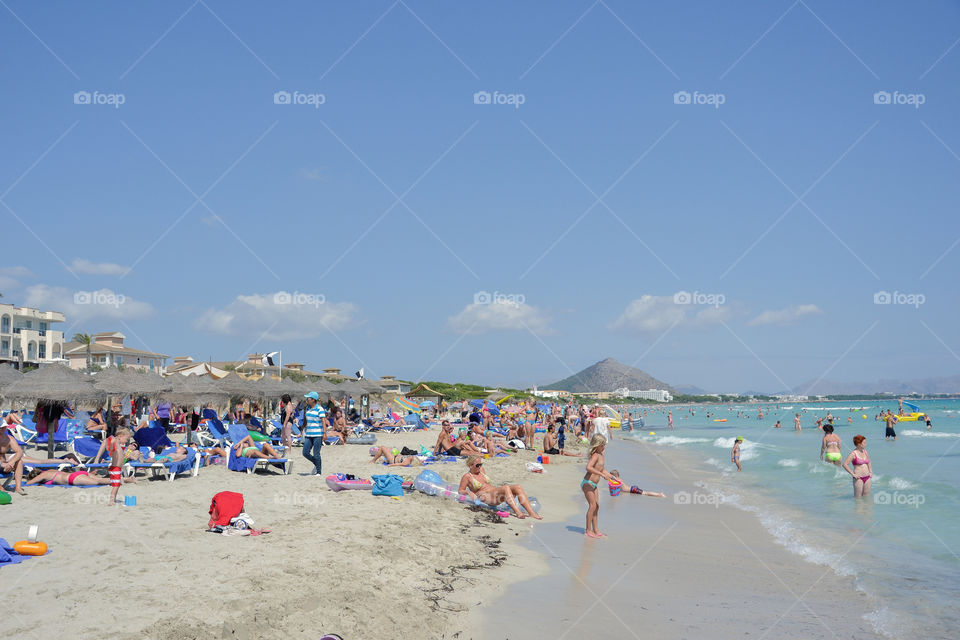 Tourists sunbathing and swimming by the beach in Alcudia on Majorca.