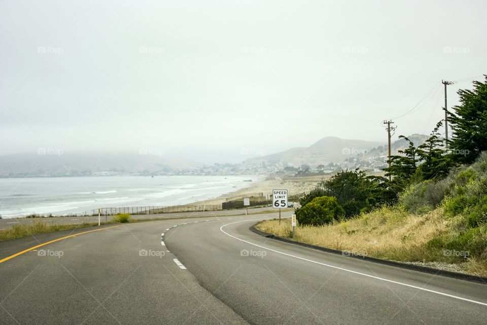 Speed limit sign reminds drivers to slow down as they curve on a Southern California coast road, Highway 1. No cars seen driving on a misty day in May.