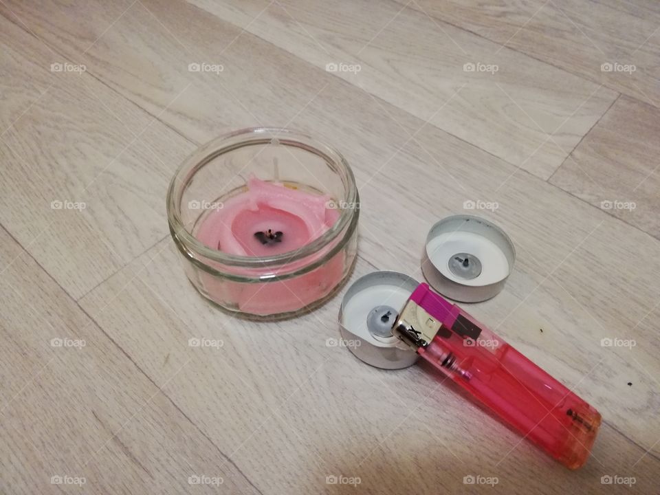 a picture of a lighter and 3 candles 1 melted in a glass bowl. on a wooden floor