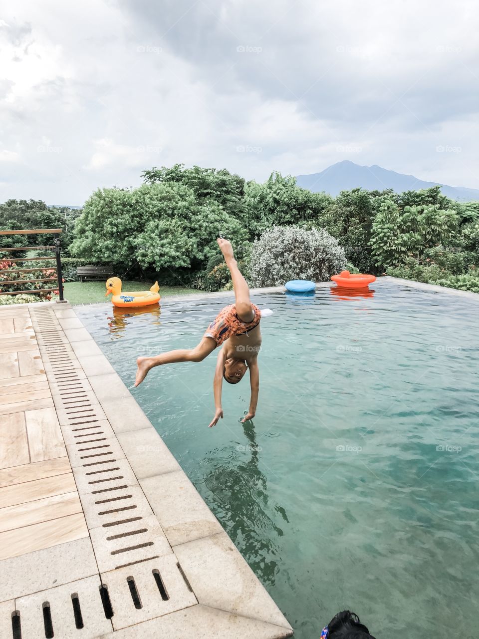 Boy doing somersault into outdoor pool with mountain in the background