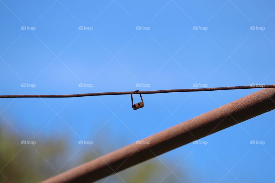 Rusted metal spring from clothespin hanging on rusted wire, conceptual minimalist, blue sky negative space 