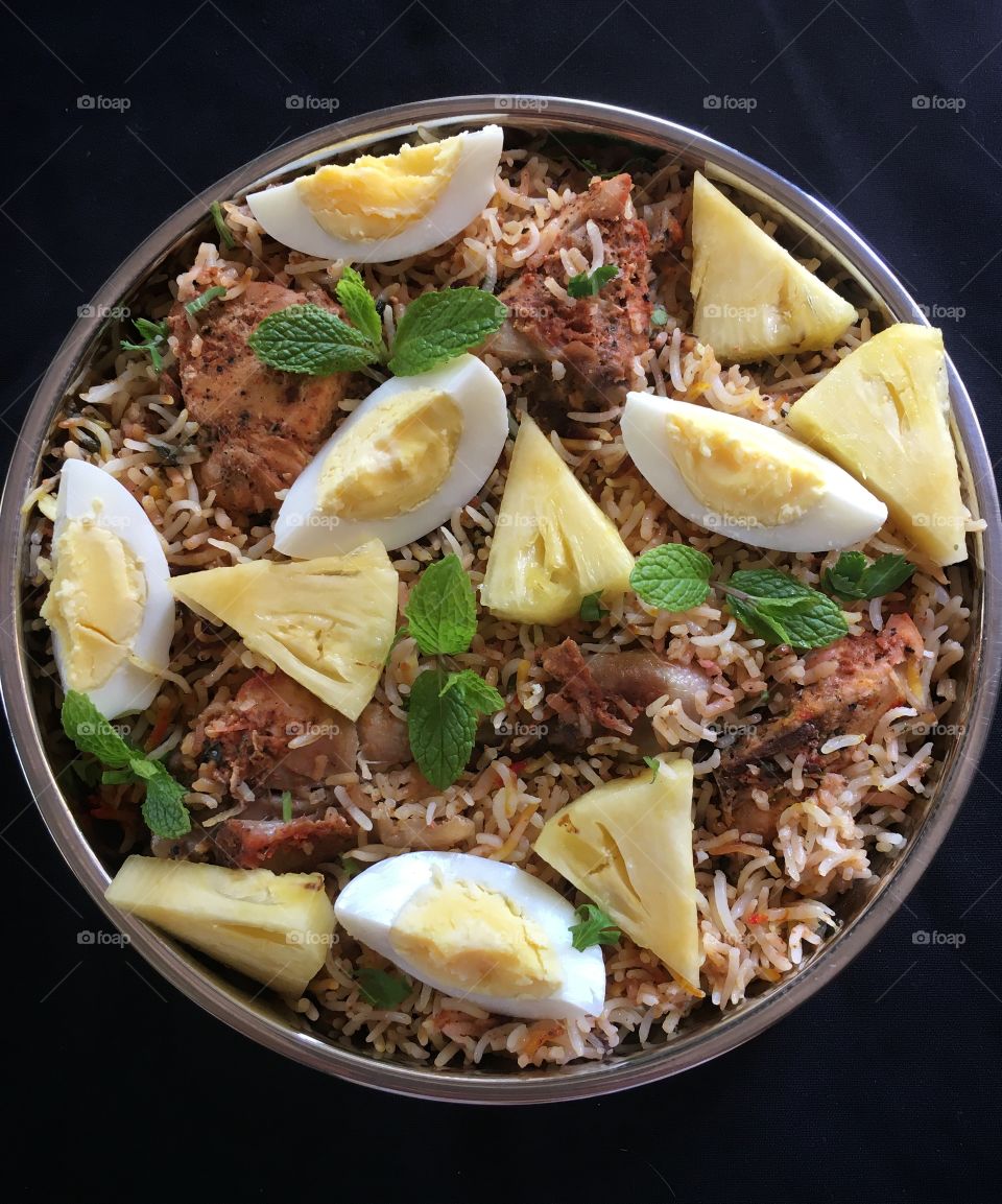 Spicy chicken biryani garnished with boiled eggs , pineapple slices and fresh mint leaves .