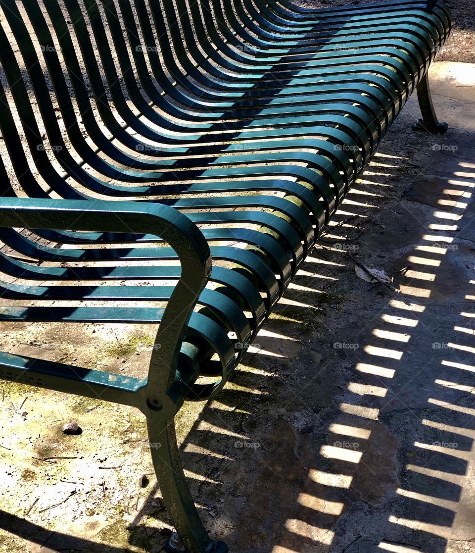 Shadow of green metal park bench 