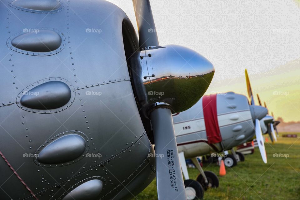Row of propeller planes parked in the grass at sunrise