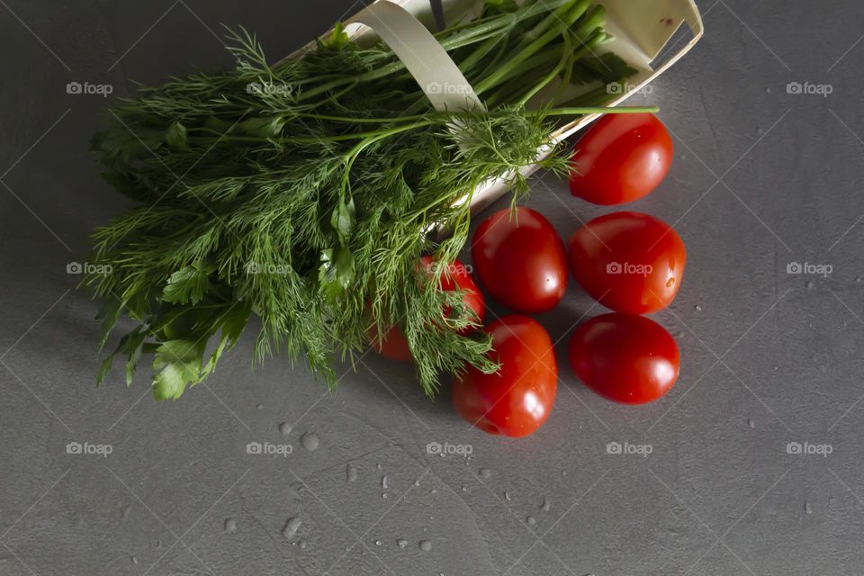 Fresh, bright, juicy vegetables and herbs for preparing salads and other vegetable dishes are in a bamboo basket on a gray, kitchen worktop.