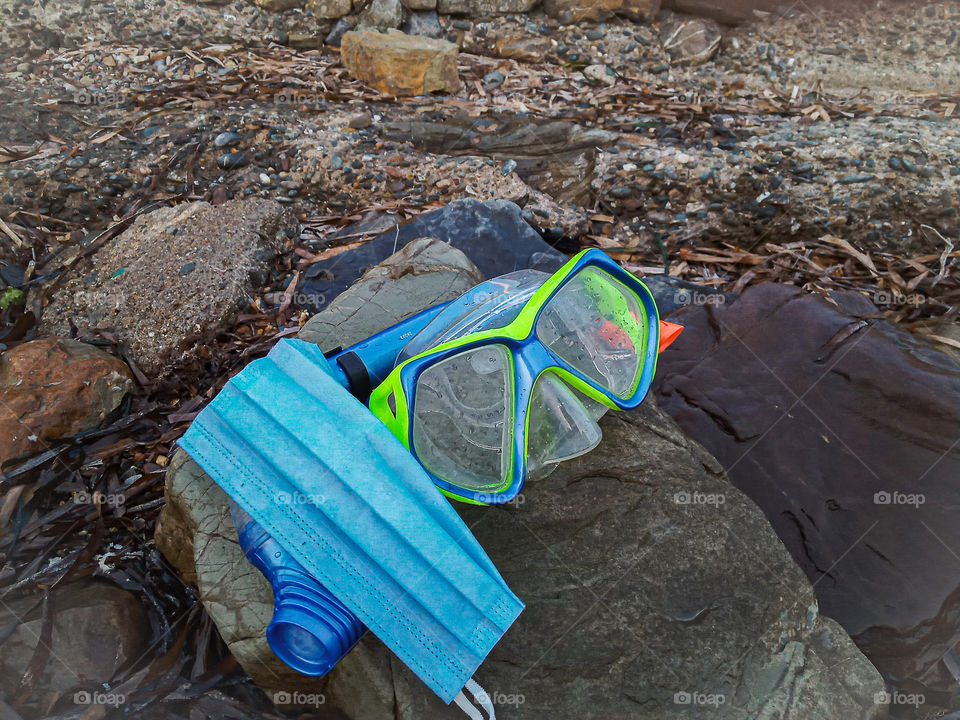 a diving mask near a surgical mask on a beach stone