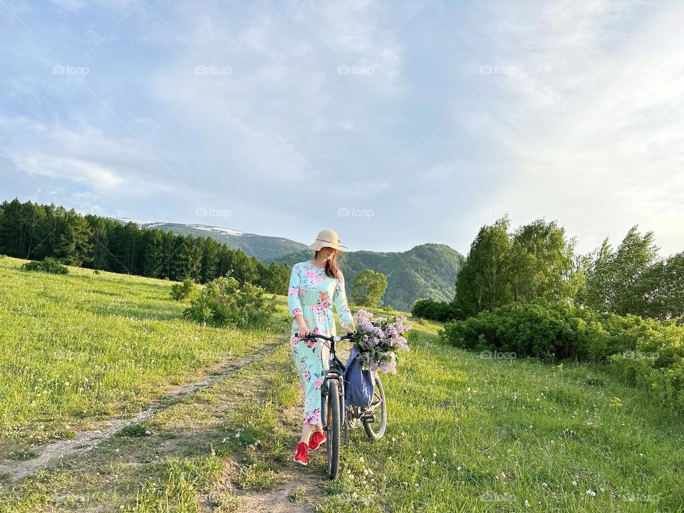 Girl in a dress with lilacs on a bicycle