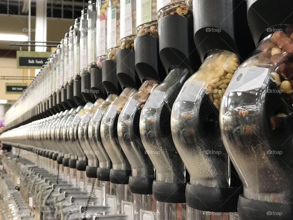 Rows of nuts and dried foods in their containers with self serve scoops in the bulk foods section of the grocery store. 