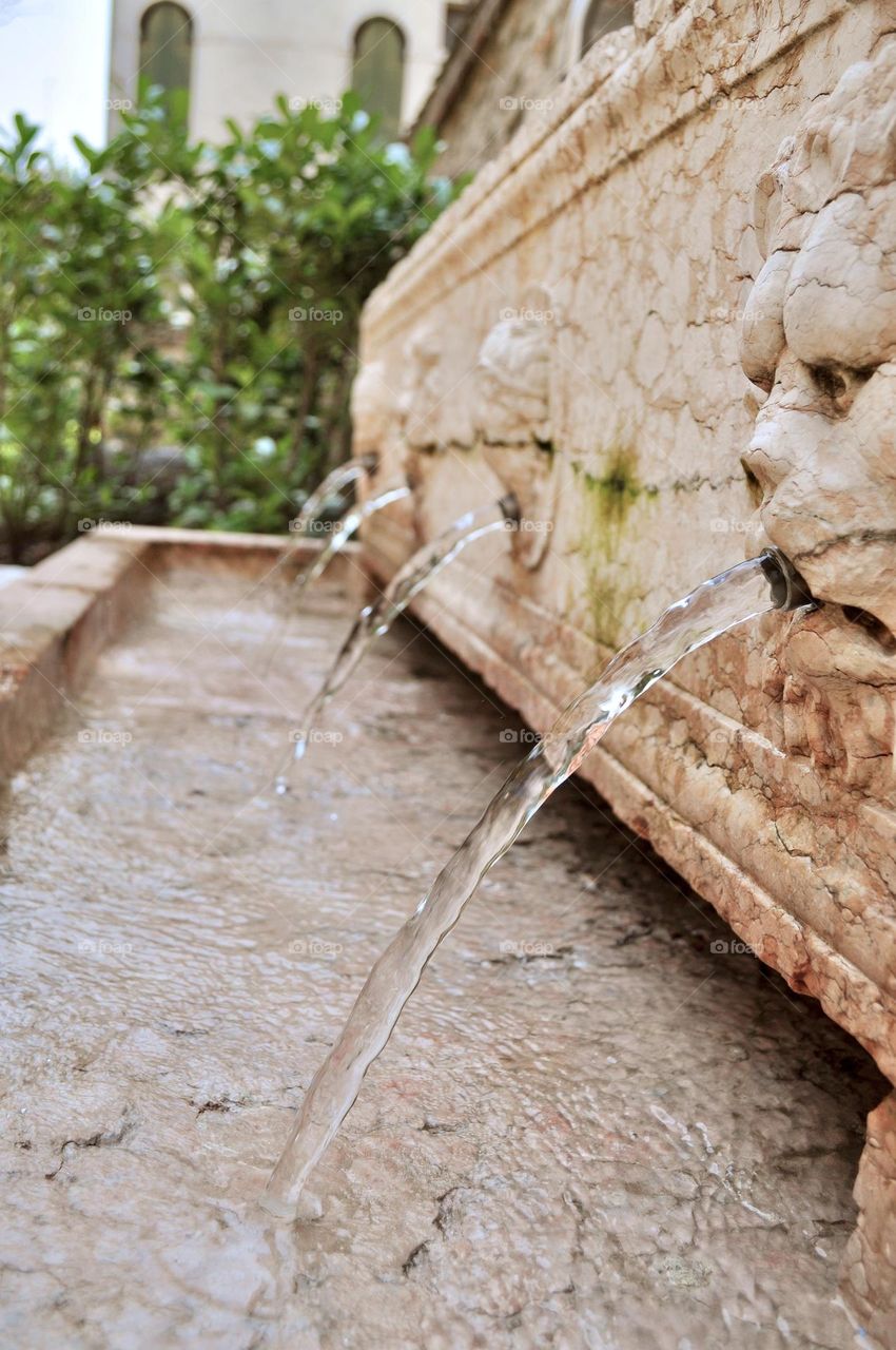 Water gushing out from lion head shaped fountains in a public garden, lion heads spurting water in a pool 