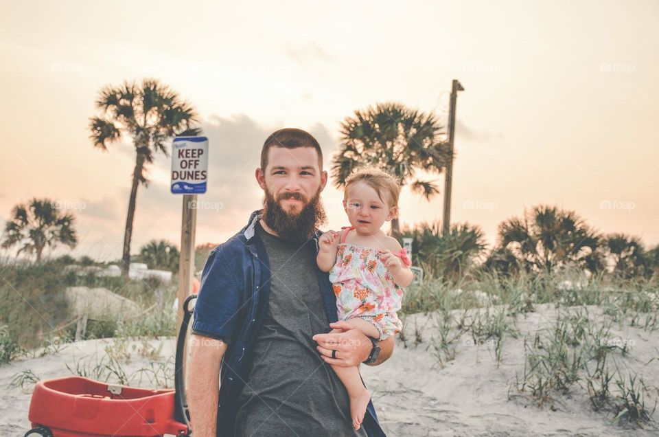 A handsome daddy holding his baby daughter at the beach 