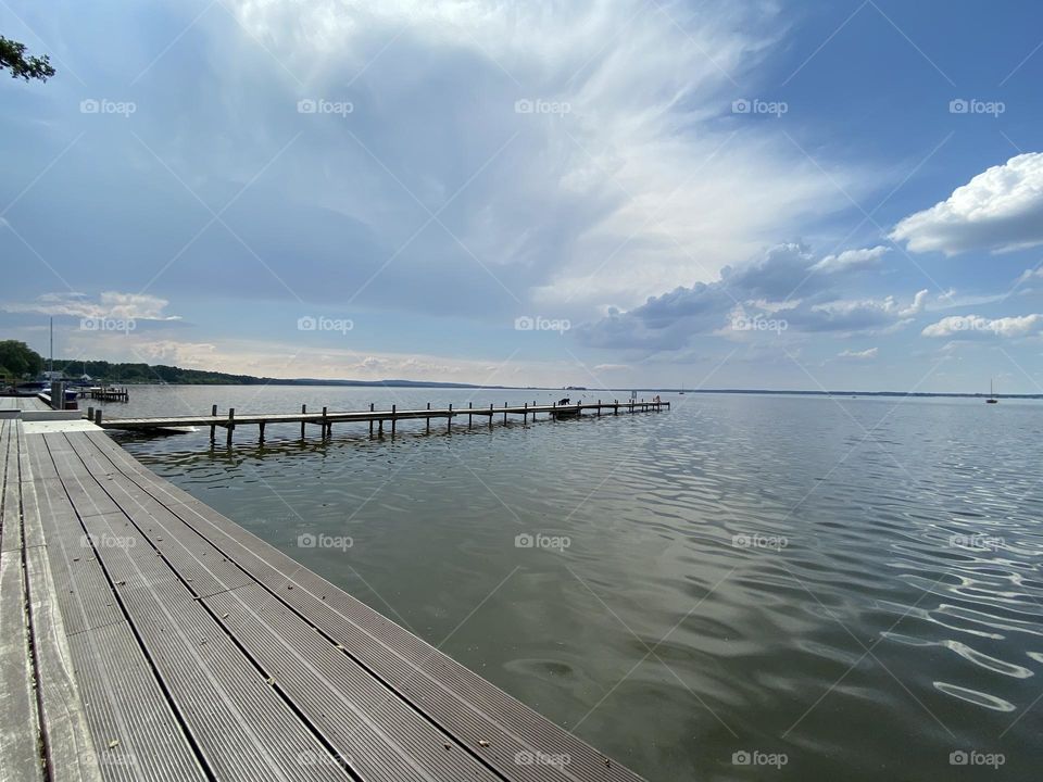 Wide angle shot of a jetty at the Steinhuder Meer with streaking clouds and slightly obscured sun.