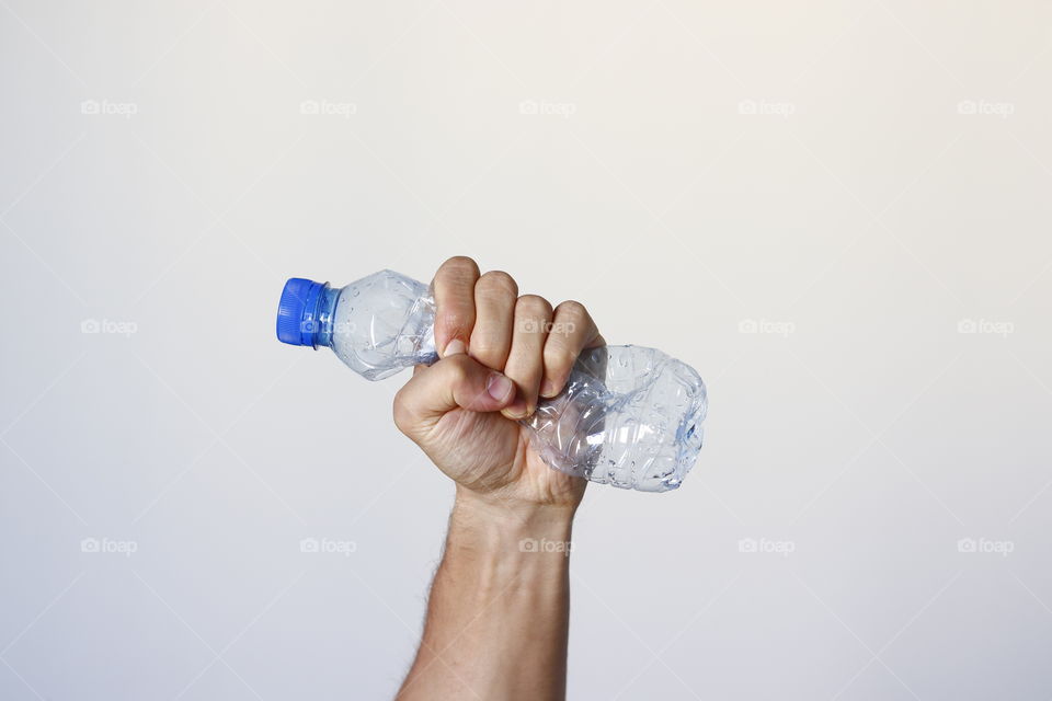 Hand squeezing pet bottle showing movement against pollution and for recycling.