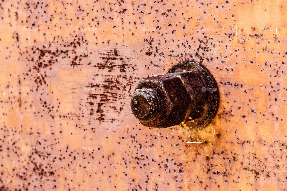 rusty orange nut and bolt and washer against a rusty iron metal plate