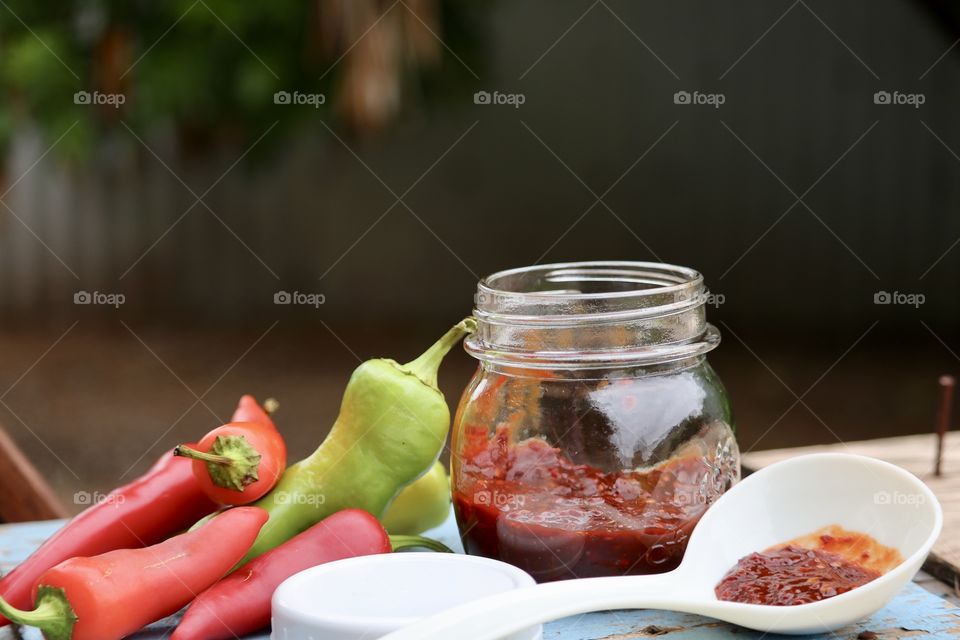 Outdoor shot pint canning jar chopped chile chili preserves, in jar and ladle and fresh peppers atop weathered wood with Bokeh blurred background 