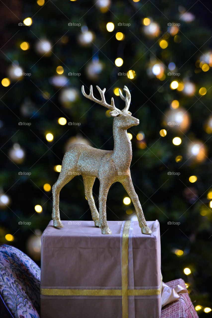 новогодняя золотая игрушка оленя на фоне огней елки