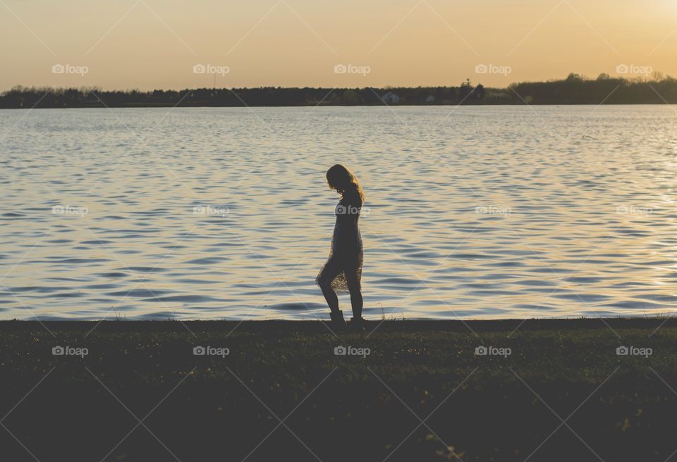 woman walking close to the lake at sunset. woman walking while thinking 