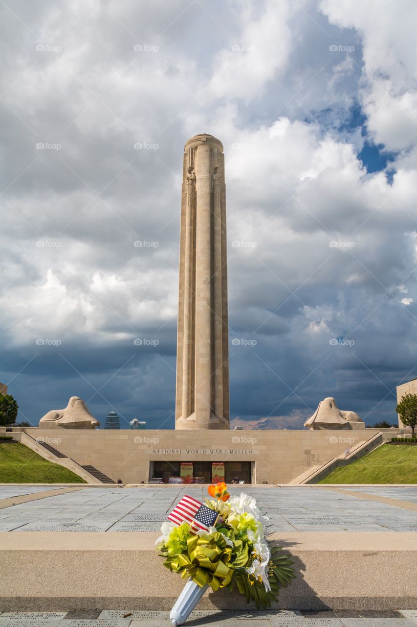Vertical low angle photo of the Liberty Memorial in Kansas City, MO with a bouquet of flowers and an American flag in the foreground (all logos and people edited out)