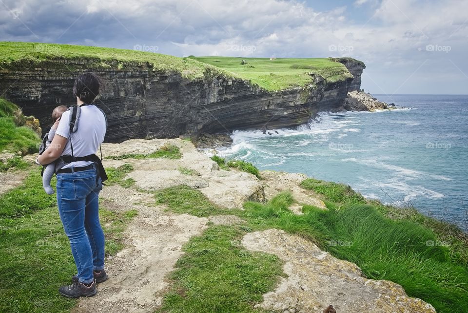 Mom with her baby in her arms looks at the cliffs