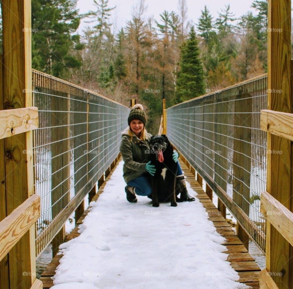 A girl and her dog, on a snowy day, on a bridge. 