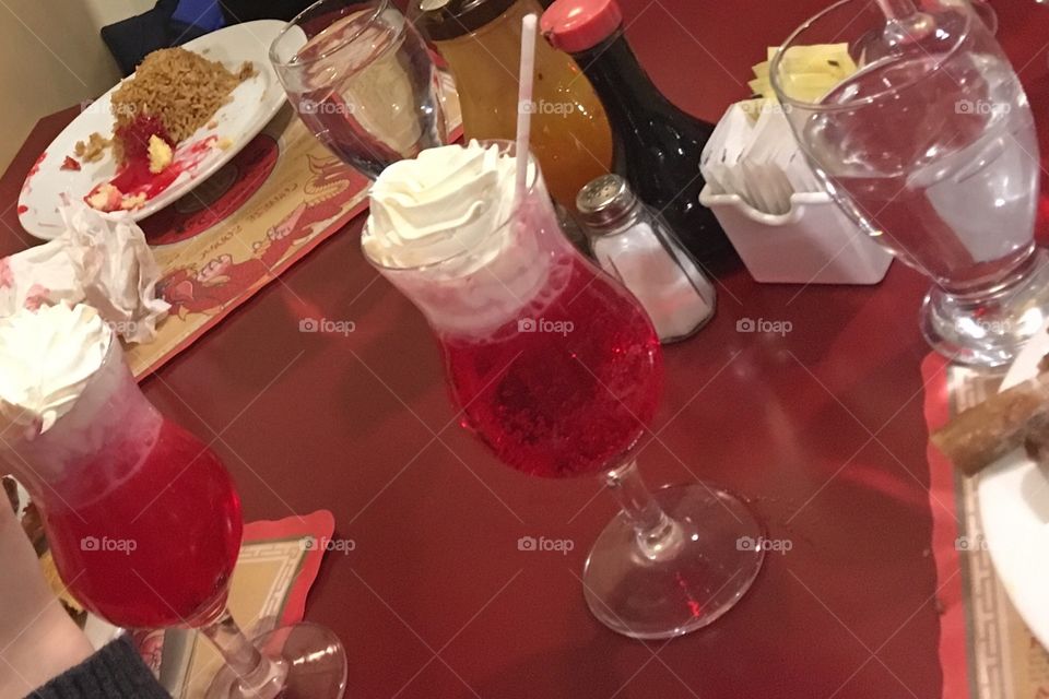 Celebrating Chinese New Year with red Shirley Temple drinks and Chinese food. Soy sauce, plum sauce and plates of food and drink on table in restaurant. 