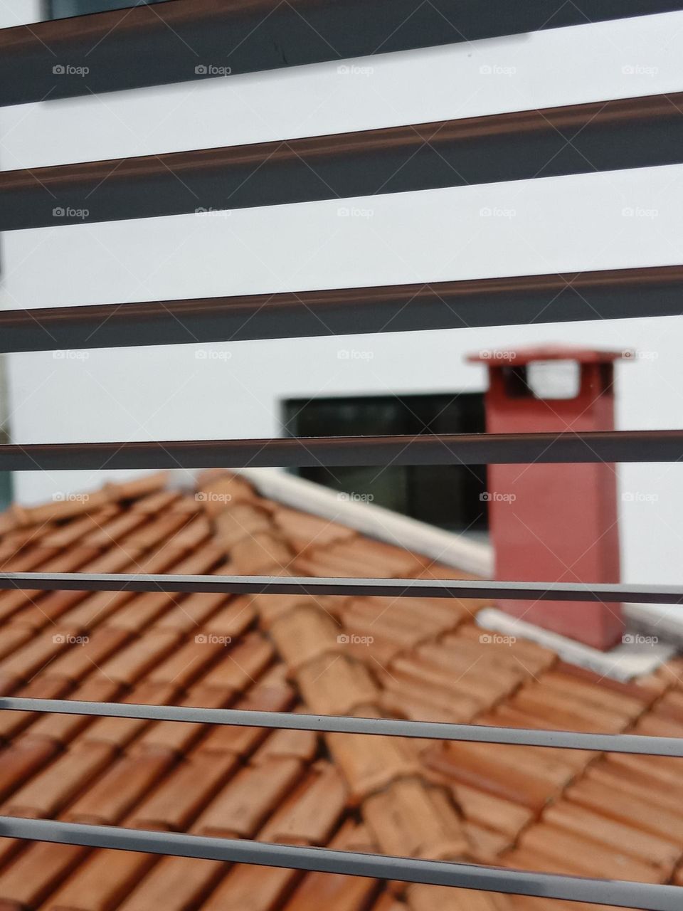 A view through the blinders,  a chimney and a tiled ceramic roof