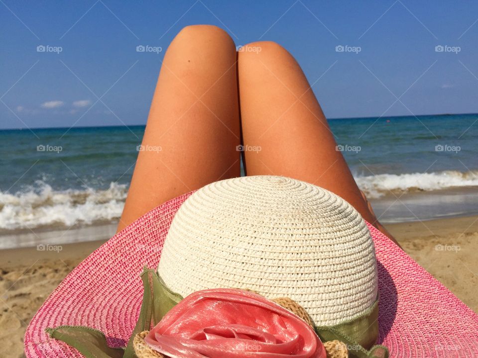 Woman legs and summer hat on the beach in Summer