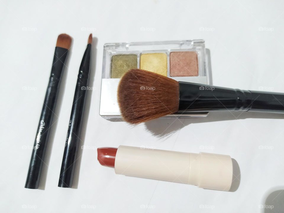 Top view, isolated on white background with lipstick, makeup brushes and eyeshadow kit