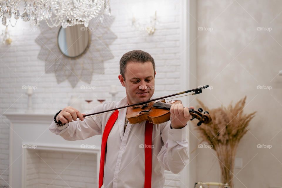 A young man plays the violin in a bright room, a musical instrument