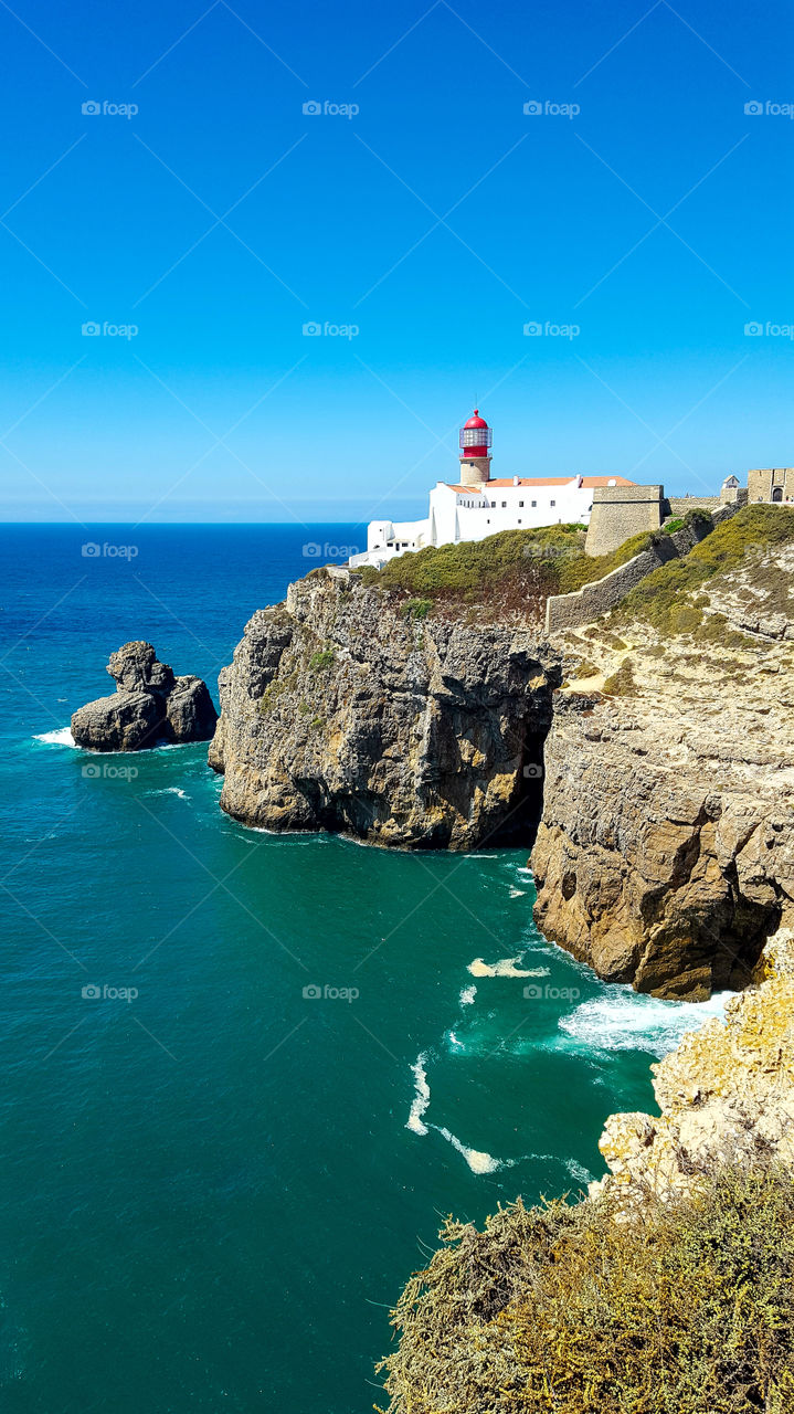 The Cabo de San Vicente Lighthouse (in Portuguese: Farol do Cabo de São Vicente) is a lighthouse located on the Cape of San Vicente, a freguesia of Sagres, council of Vila do Bispo, Algarve region, Portugal. It is built inside the Fortress of San Vicente of the sixteenth century. The headlight emits a flash of white light of 0.1 s of duration every 5 seconds. It has a nominal night range of 32 nautical miles. During the reign of Manuel I of Portugal, at the beginning of the 16th century, the Bishop of Algarve, Fernando Coutinho, ordered a fortress and a tower to be built on the Cape of San Vicente as a beacon as a defense of that area of ​​the coast. In 1587, the British pirate Francis Drake destroyed the fort and the primitive lighthouse. The structure was ordered to be rebuilt by King Felipe II of Portugal, (III of Spain) in 1606. Like all the fortresses in the area, it was razed during the earthquake of 1755.