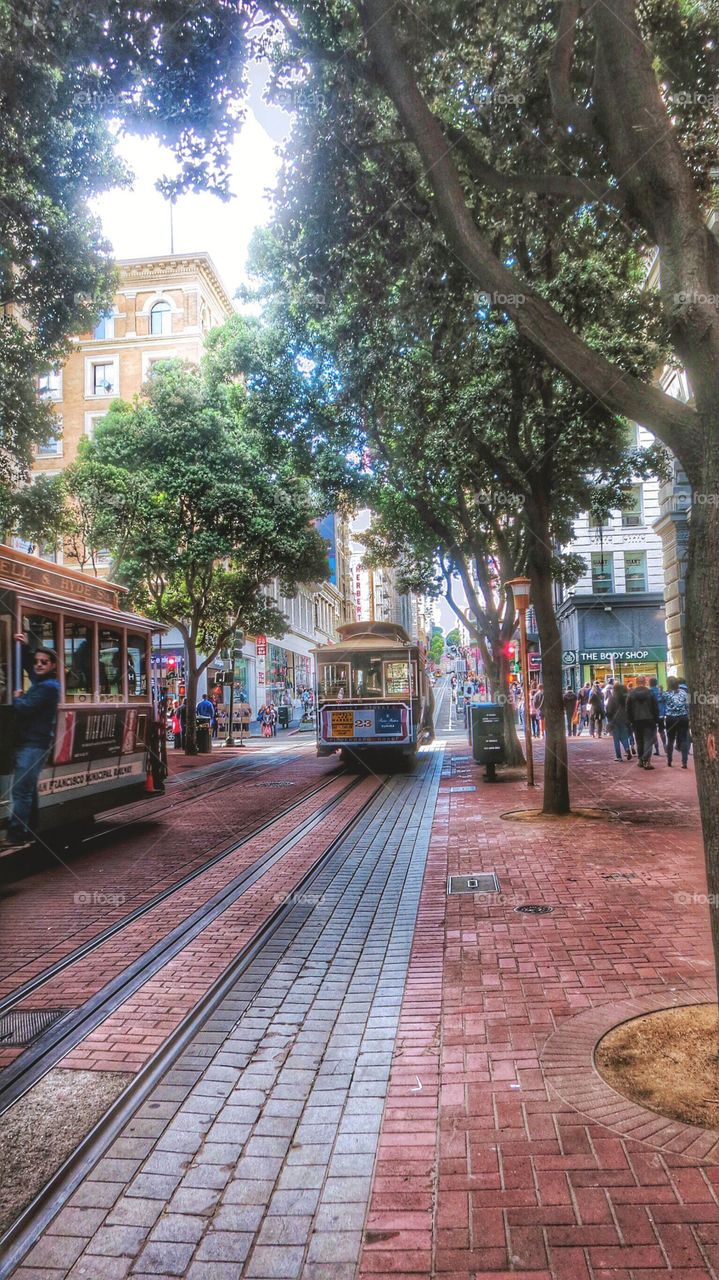A street scene in San Francisco of a cable car  and hustle and bustle of people around the town.