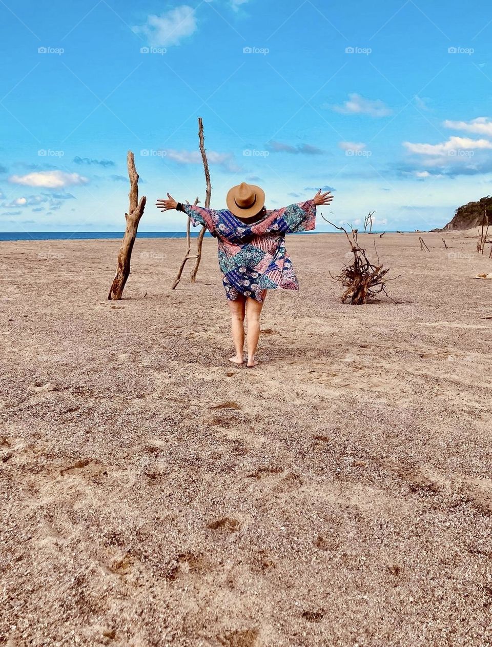 A beautiful woman poses with arms wide open in front of various driftwood on Lo De Marcos beach in Nayarit, Mexico.